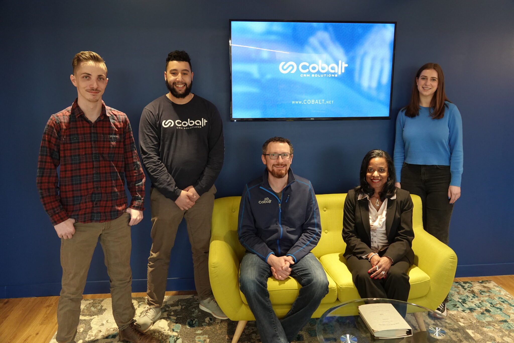 The image is a group photo of Cobalt's support team for associations in the lobby of their Washington D.C. office. Training and support are one of the significant factors that affect AMS cost over time.